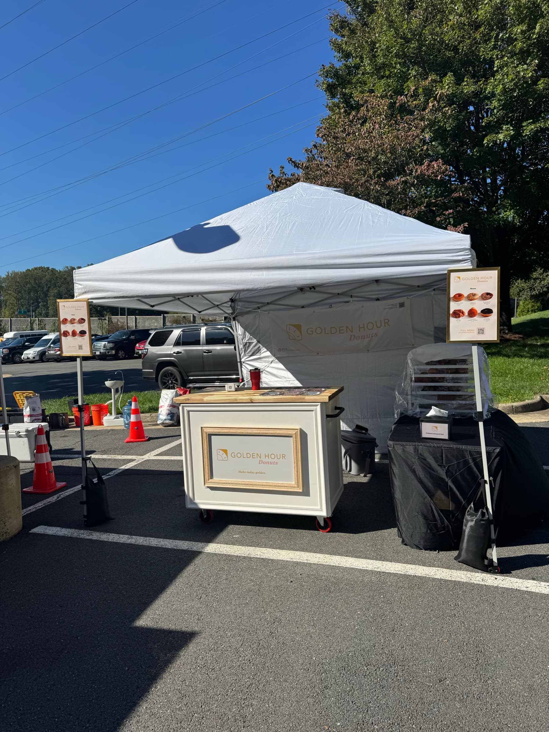 The Golden Hour donut cart and tent set up for an event, with menu boards on either side